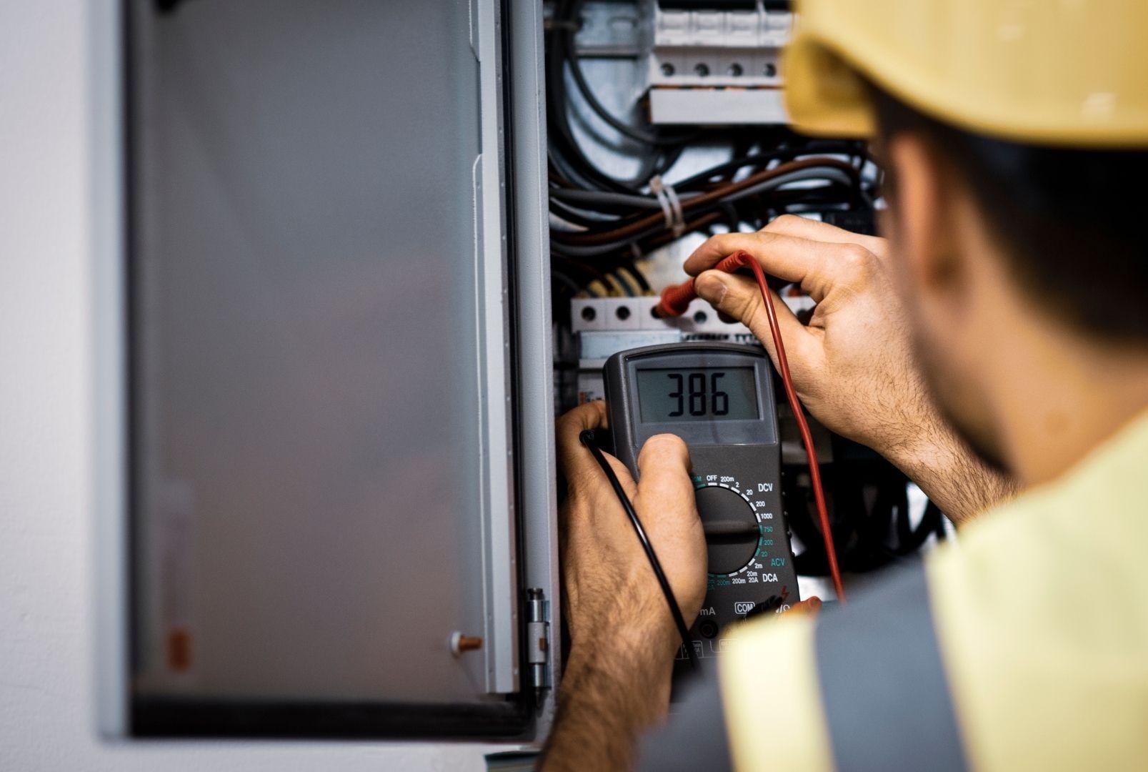 A man is using a multimeter to test an electrical box.