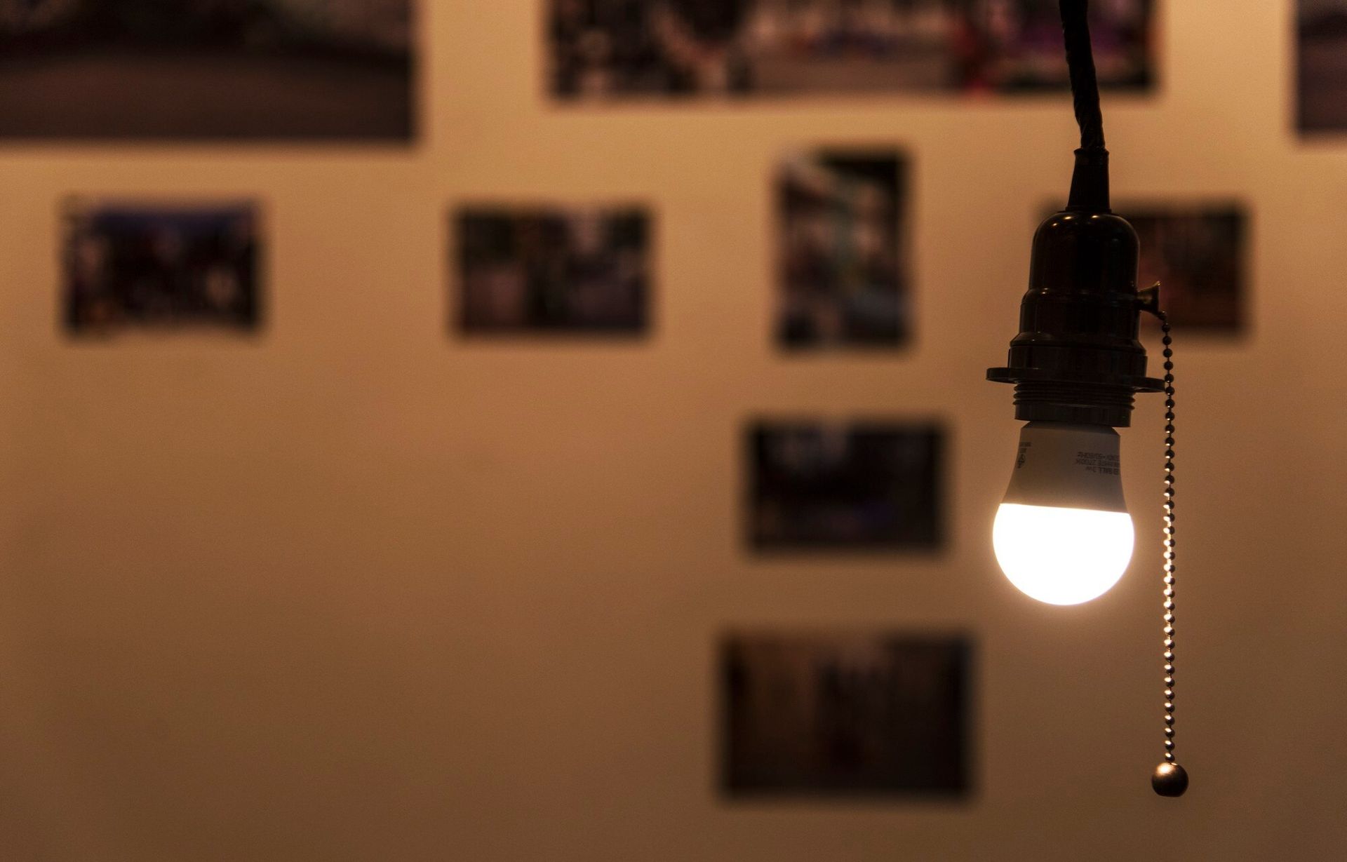 A light bulb is hanging from the ceiling in front of a wall of pictures.