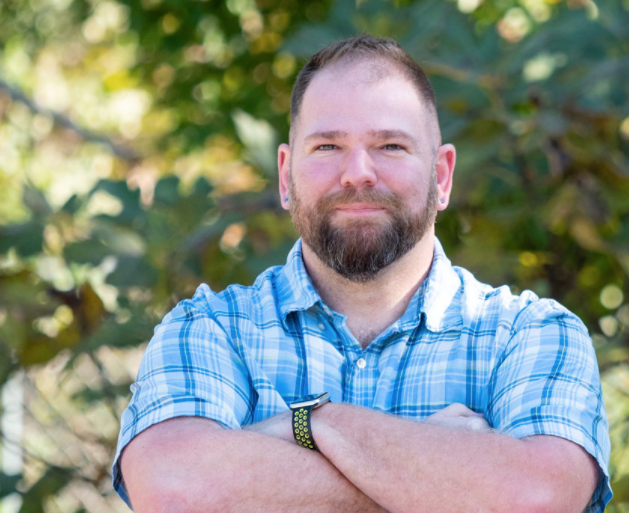 Branson, Brookline Homes team member, headshot outdoors at a home construction site with arms crossed
