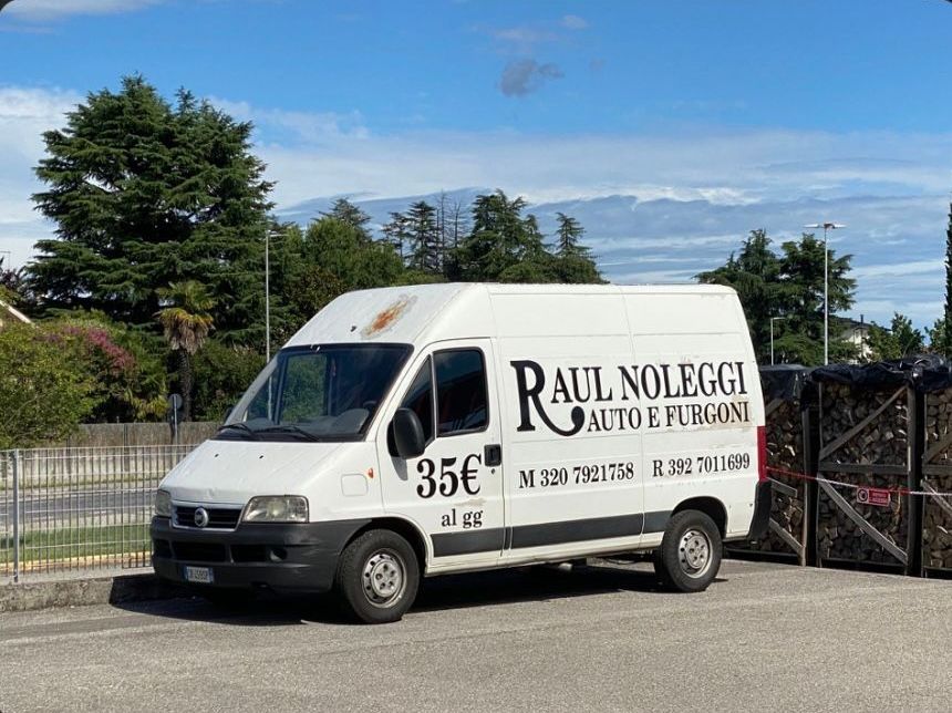 Un'auto verde è parcheggiata su un vialetto di mattoni davanti a una recinzione.