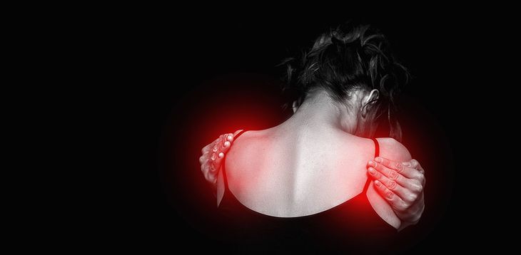 A woman is holding her shoulder in pain.