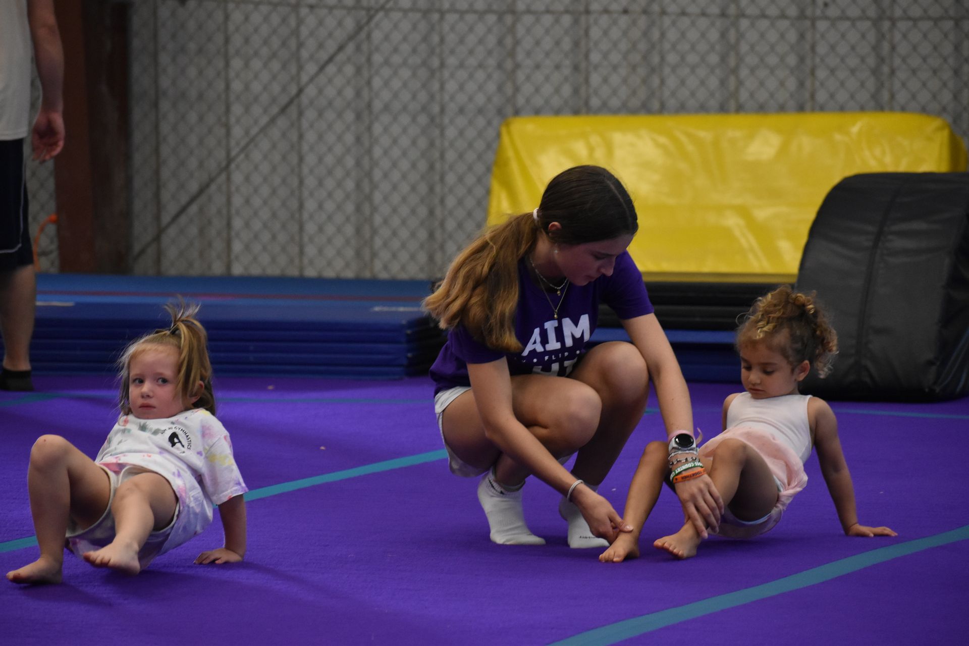 Young gymnast and instructor on a purple mat; instructor helping girl with her skills.