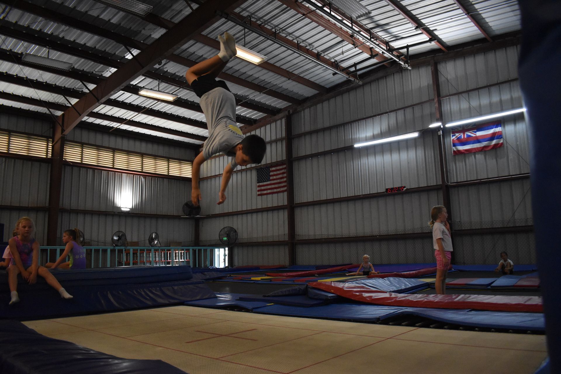 Boy doing a backflip on a trampoline indoors, with other children in the background.