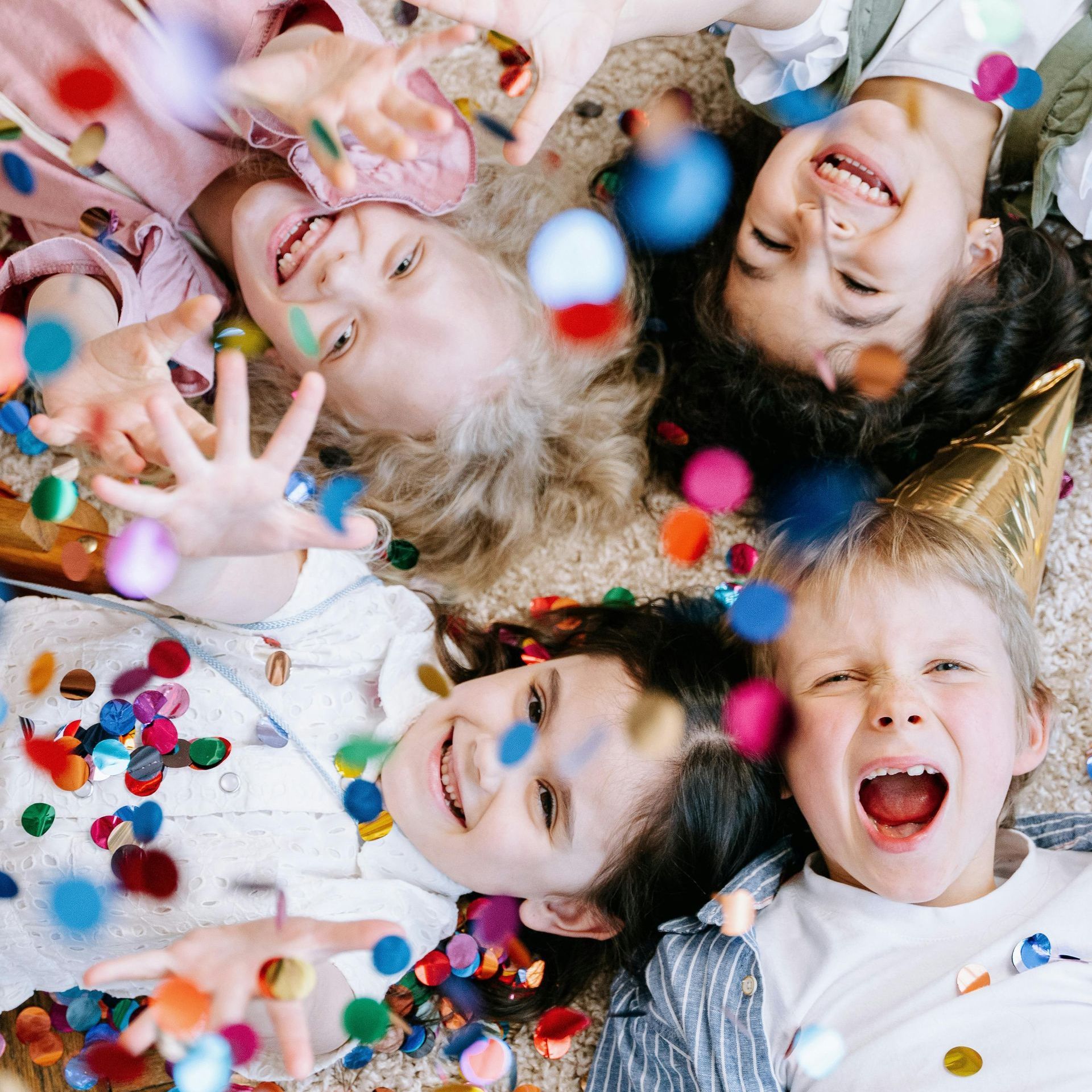 A group of children are laying on the floor with confetti falling around them.