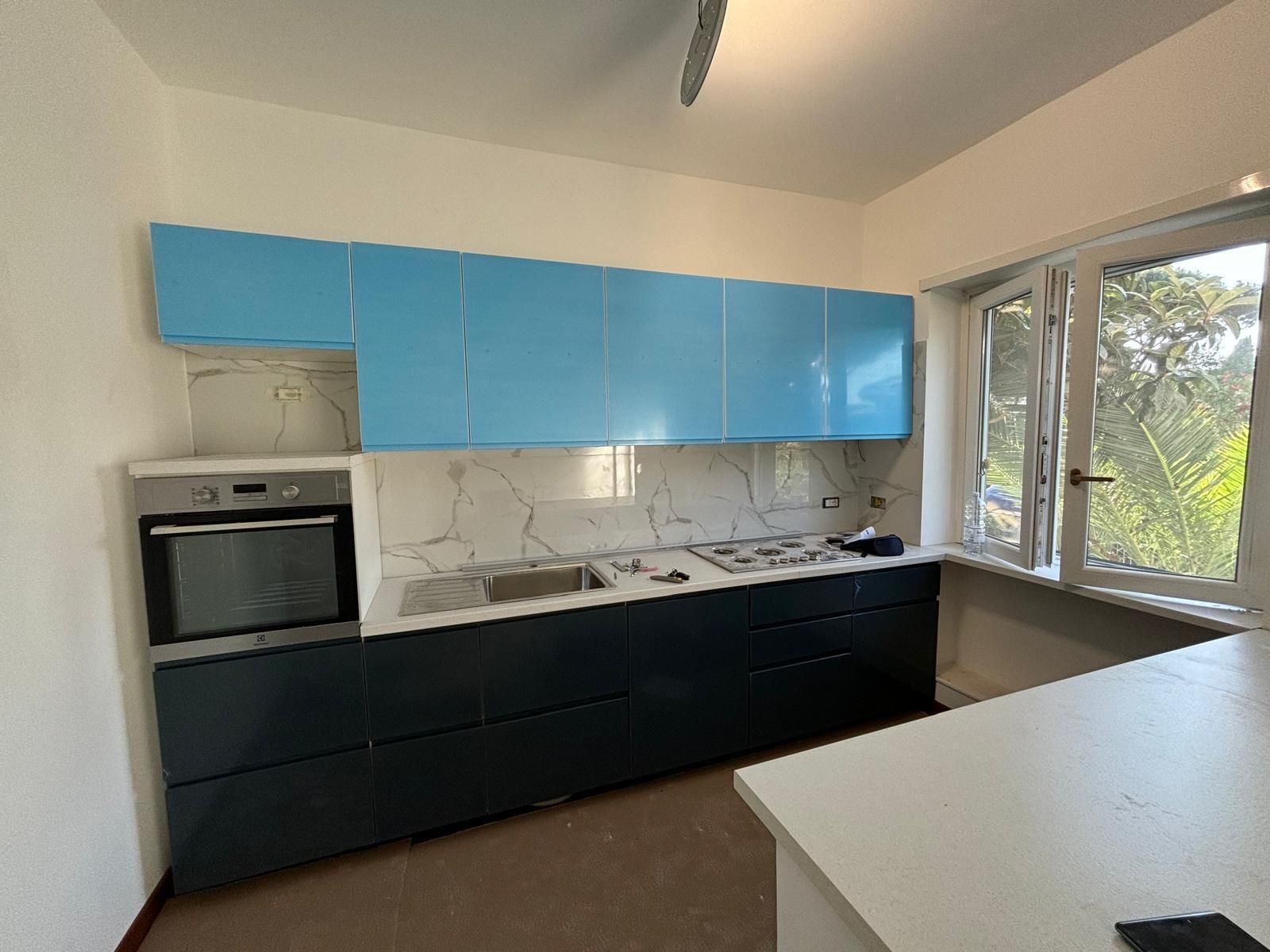 Una cucina con mobili blu, una stufa, un lavandino e una finestra.