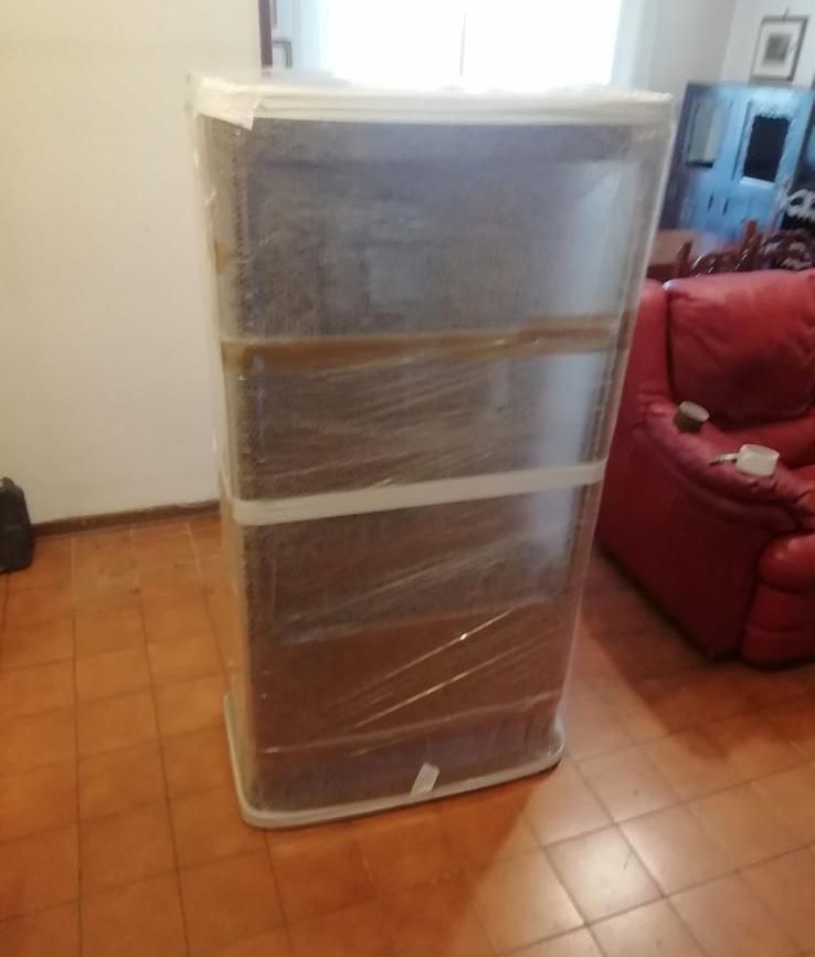 Una grande scatola avvolta nella plastica si trova in un soggiorno accanto a una sedia rossa.