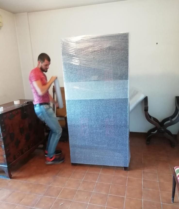 Un uomo è in piedi accanto a una grande scatola avvolta nella plastica in un soggiorno.