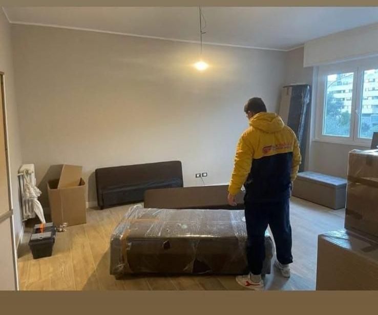 Un uomo con una giacca gialla è in piedi accanto a un letto in un soggiorno.