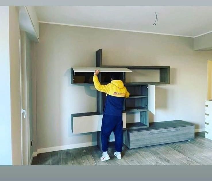 Un uomo con una giacca gialla sta aprendo uno scaffale in un soggiorno