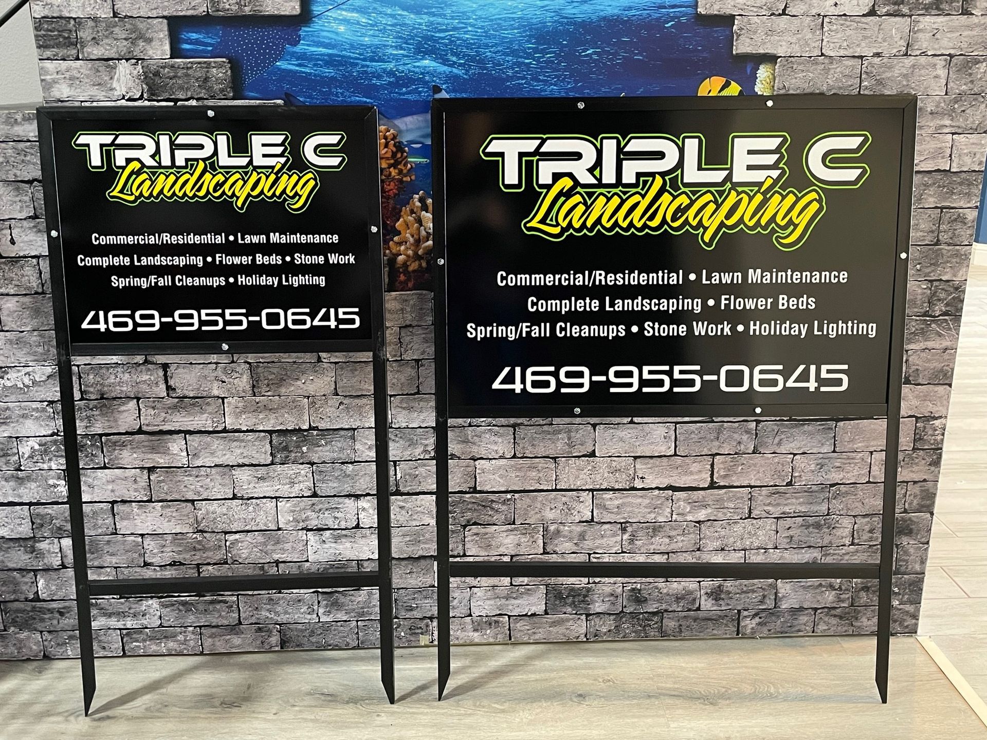 Two signs for triple c landscaping are displayed in front of a brick wall