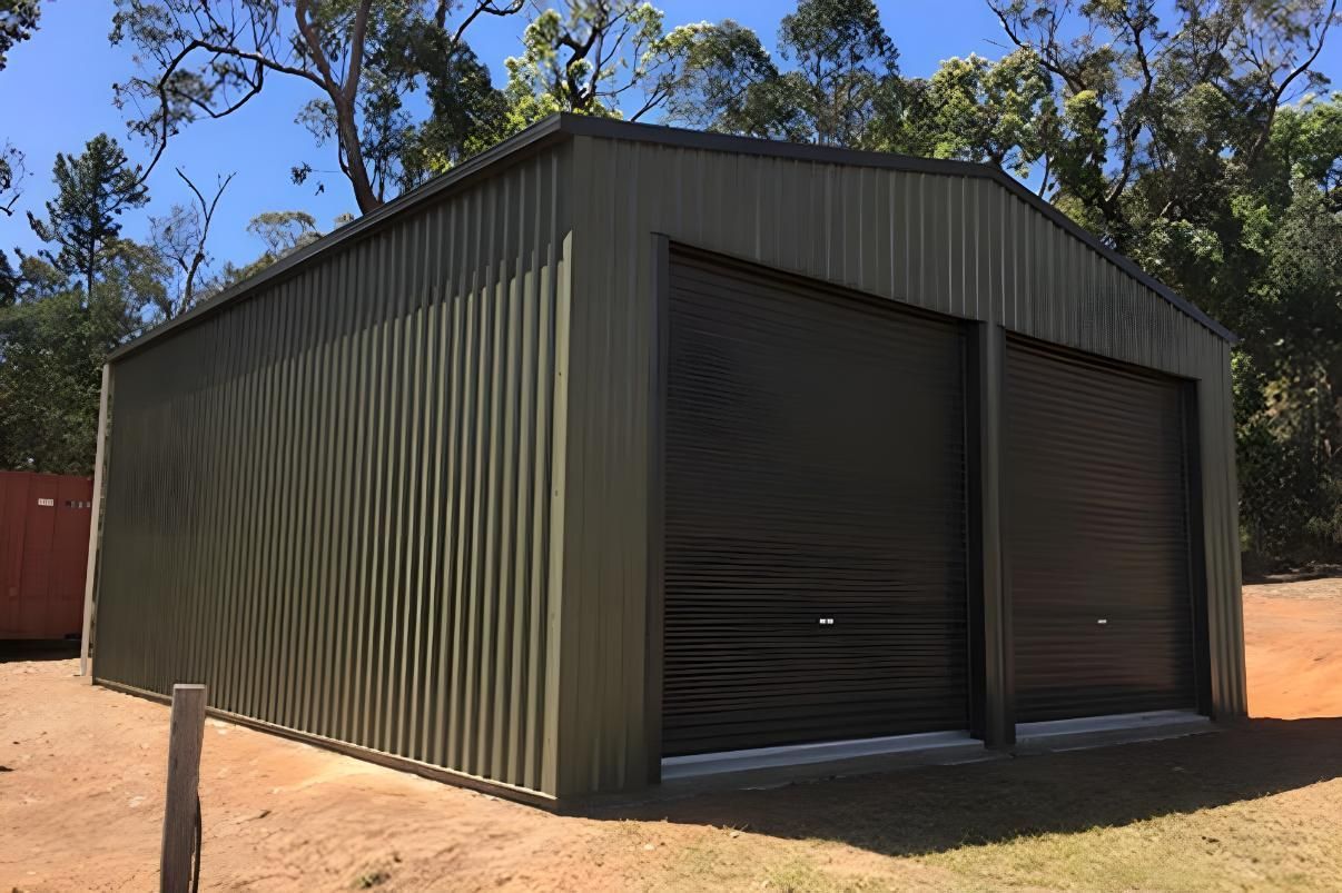 A Green Metal Building With Two Garage Doors Is Sitting In The Middle Of A Field — Dunnrite Mareeba Sheds & Garages In Mareeba, QLD
