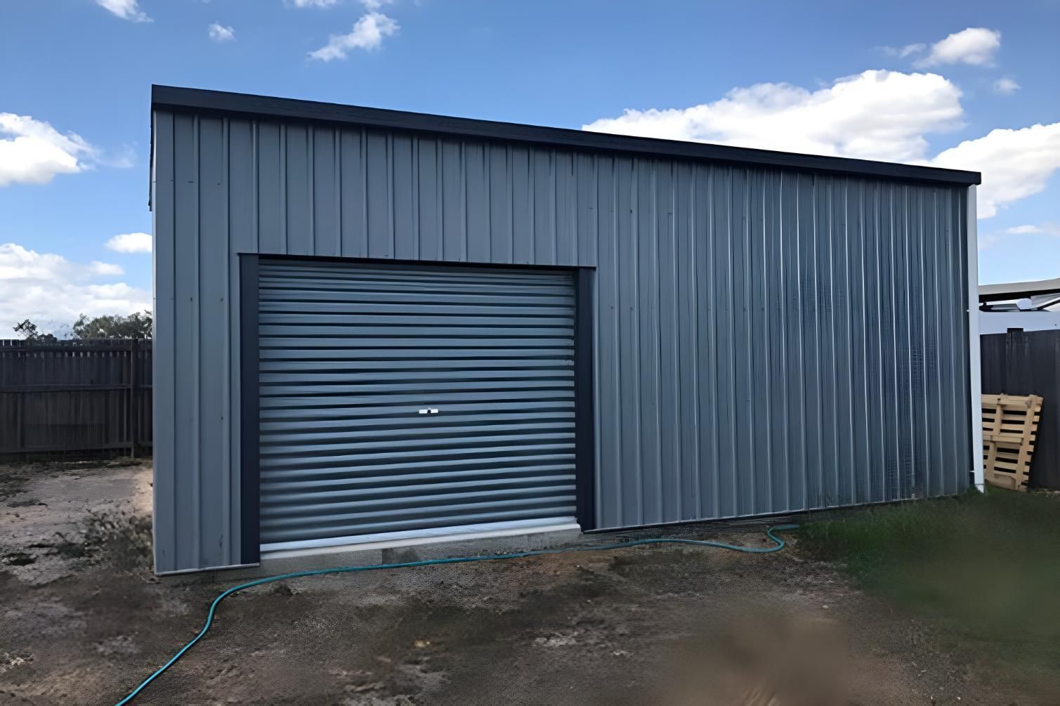 A Gray Metal Building With A Garage Door And A Hose Attached To It — Dunnrite Mareeba Sheds & Garages In Mareeba, QLD