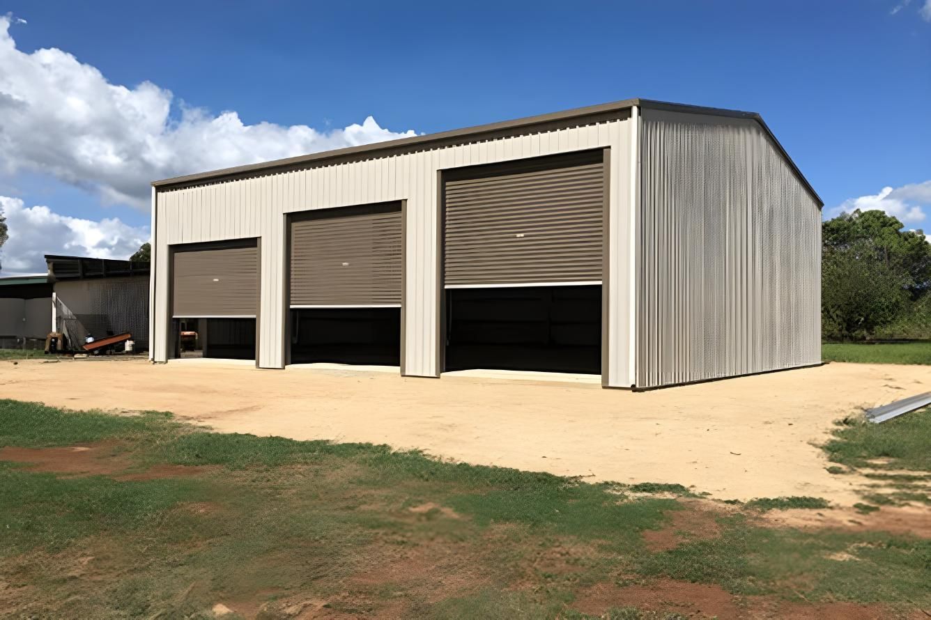 A Large Metal Building With Three Garage Doors Is Sitting On Top Of A Dirt Field — Dunnrite Mareeba Sheds & Garages In Mareeba, QLD