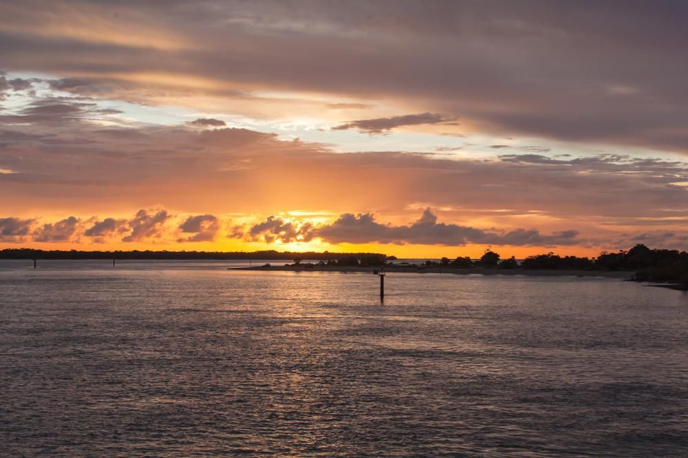 A Sunset Over A Body Of Water With A Cloudy Sky — Dunnrite Mareeba Sheds & Garages In Weipa, QLD