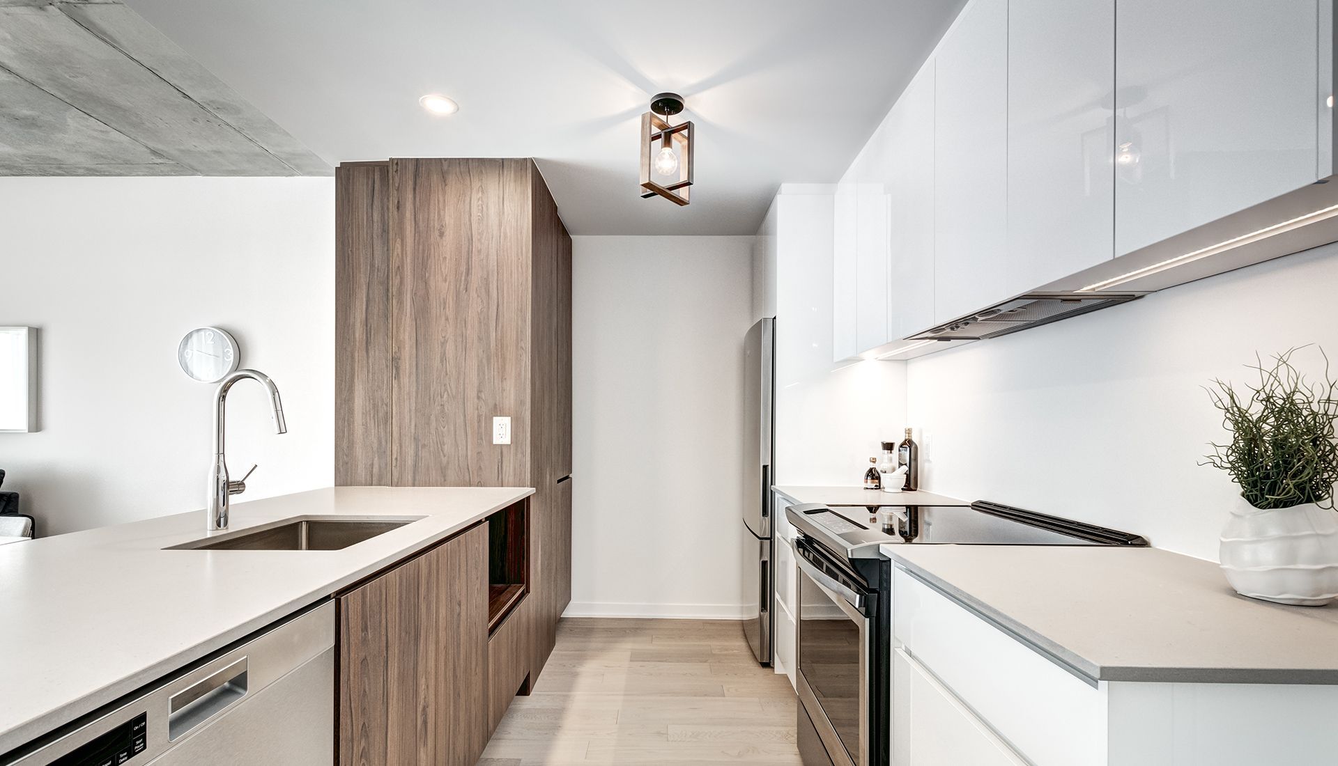 Modern kitchen: white countertops, wood cabinetry, stainless steel appliances, recessed lighting, and a decorative light fixture.