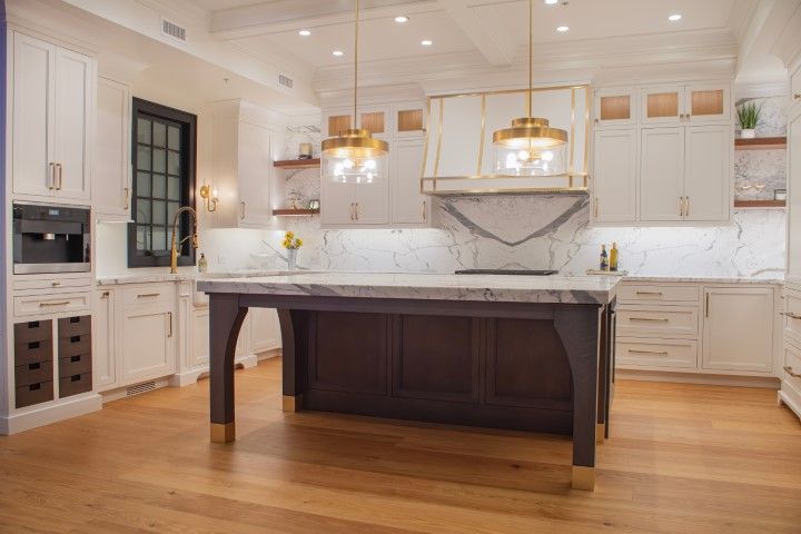 Luxurious white kitchen with marble countertops, dark island, and gold accents.