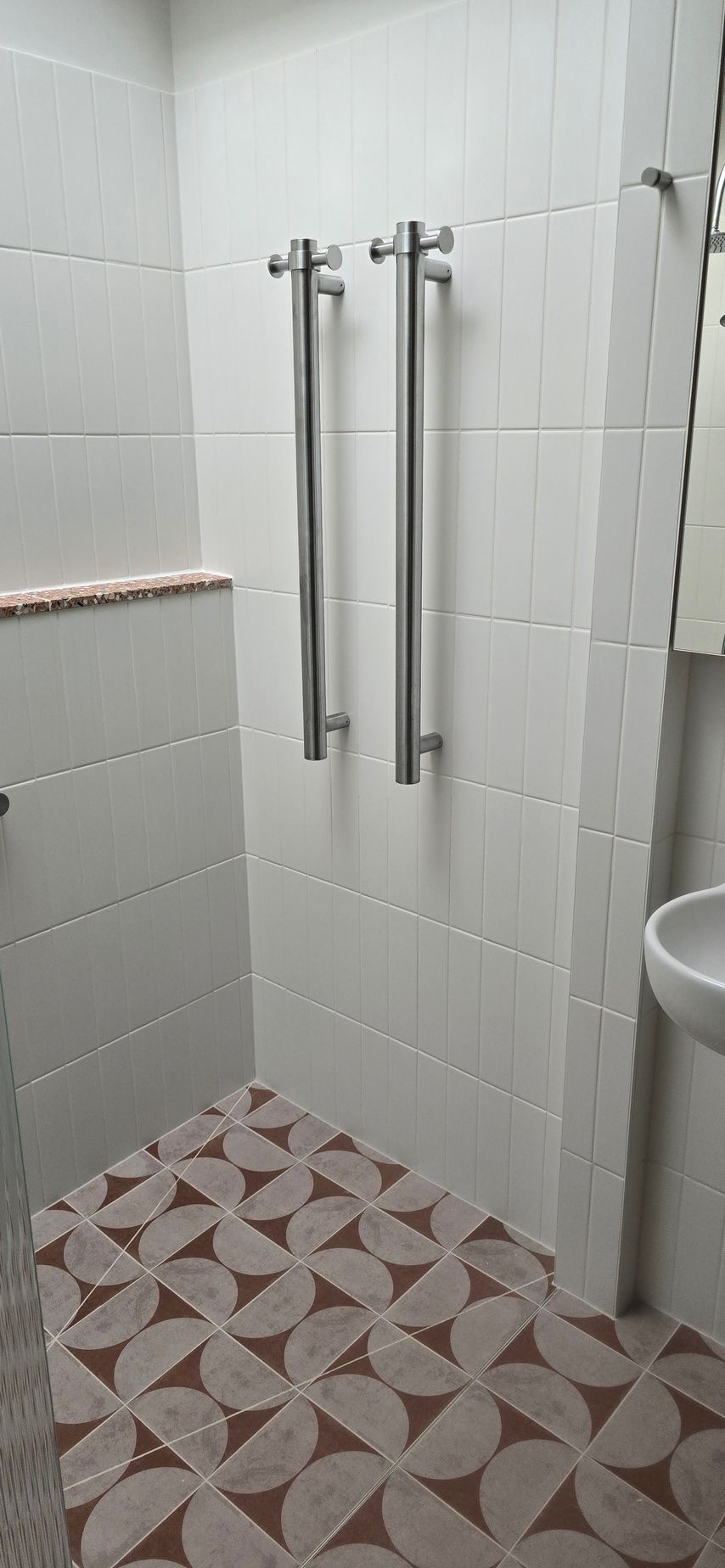 A bathroom with a walk in shower , sink and towel rack.
