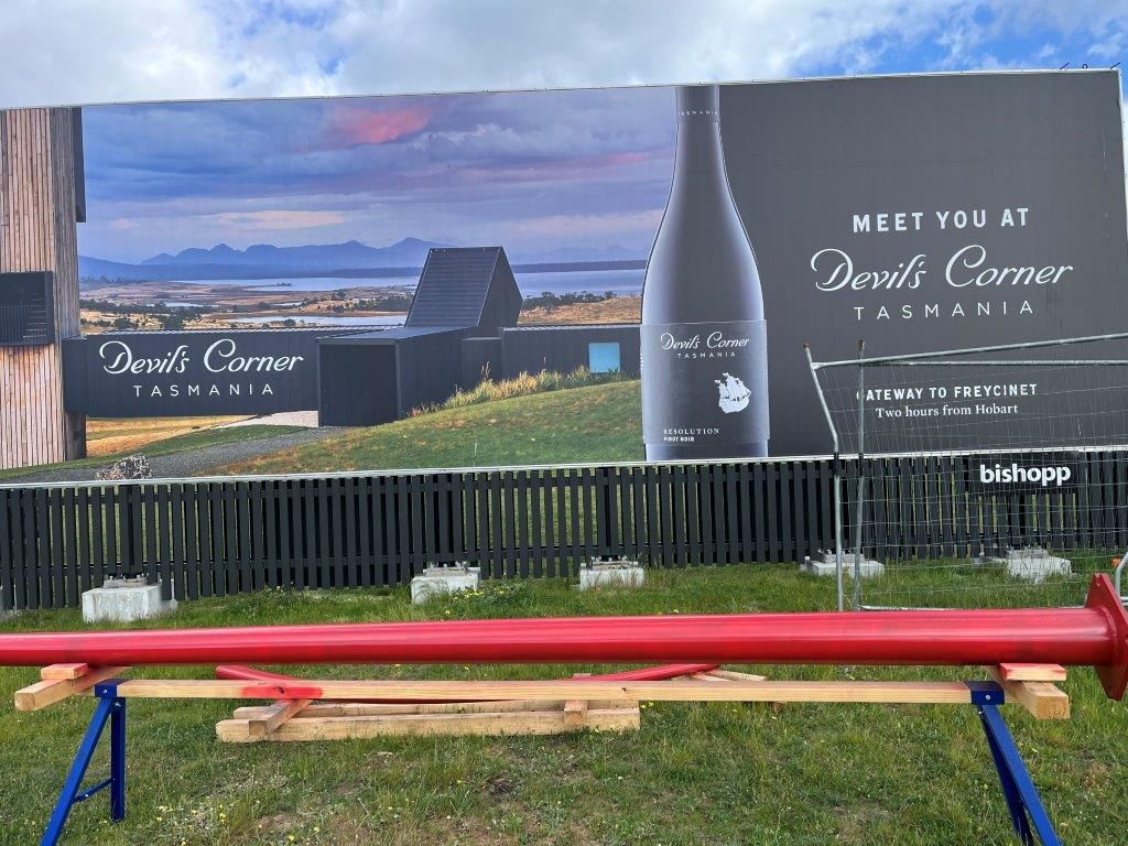 A large billboard with a bottle of wine on it is sitting in the grass.