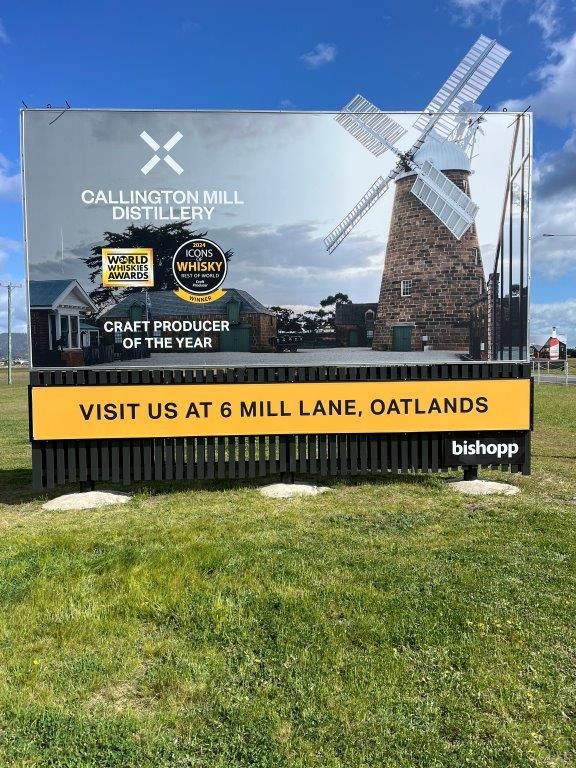 A large billboard with a windmill on it is in the middle of a grassy field.