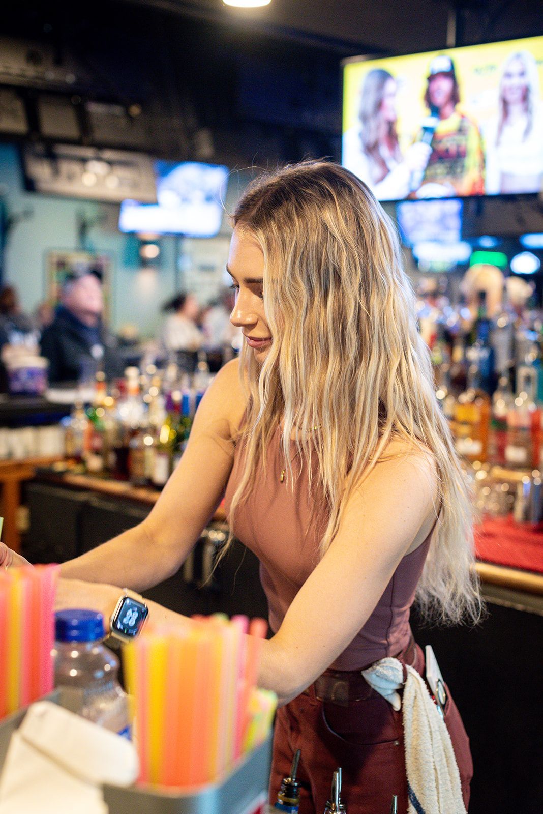 A woman is standing at a bar preparing drinks.