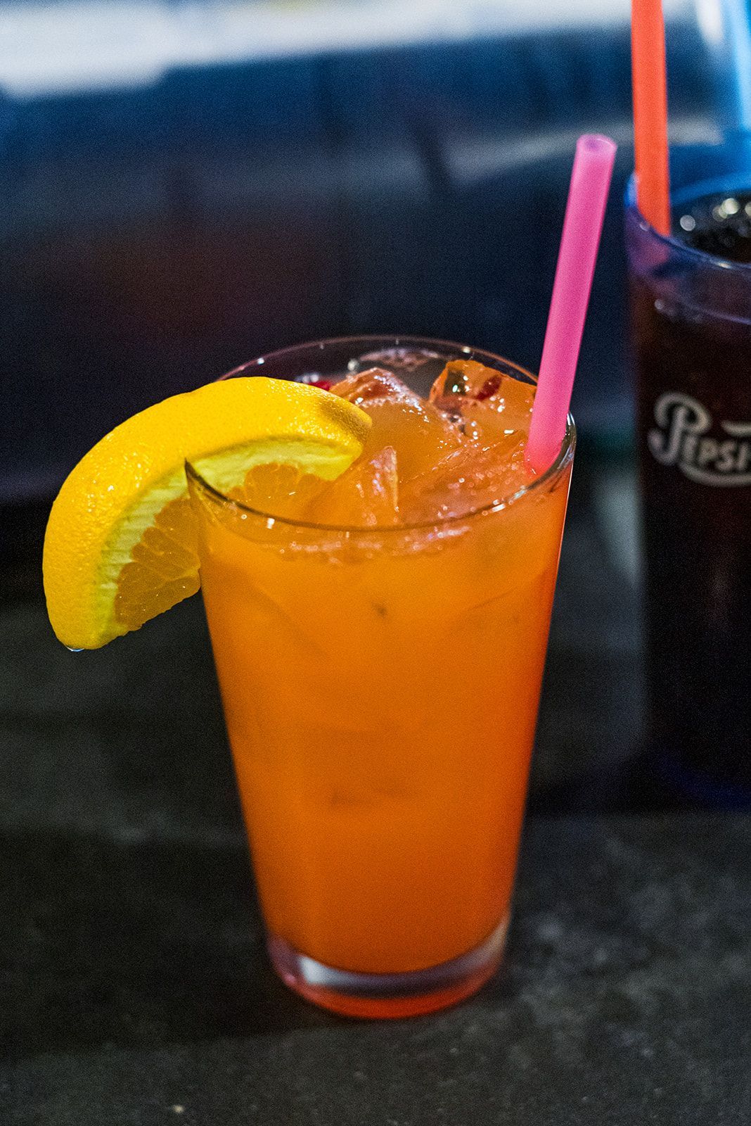 A glass of orange liquid with a lemon slice and a pink straw