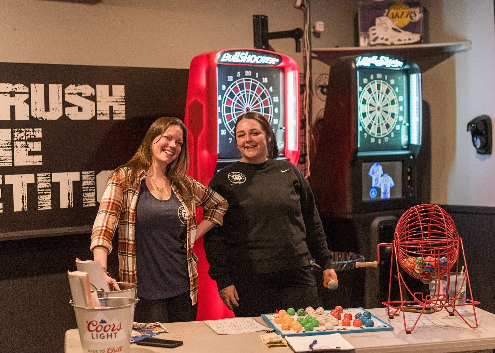 Two women are standing next to each other in front of a dart board.