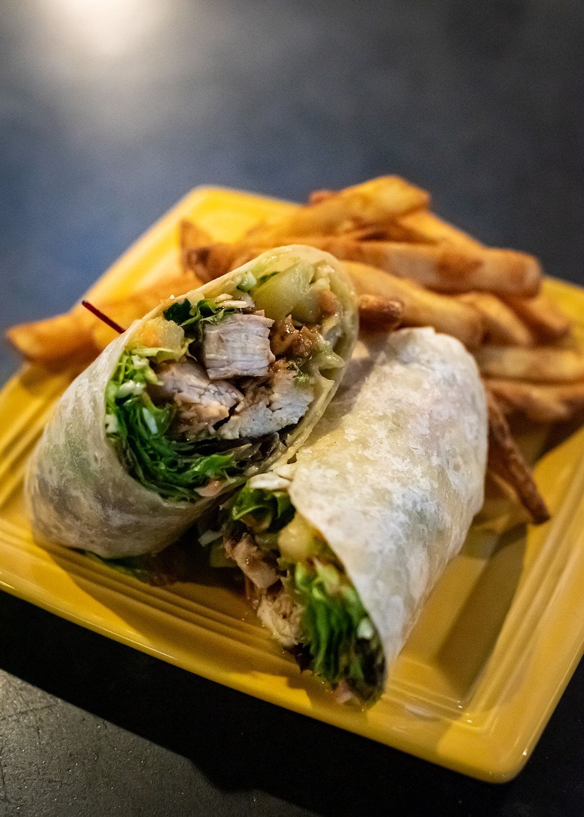 A chicken wrap and french fries on a yellow plate.