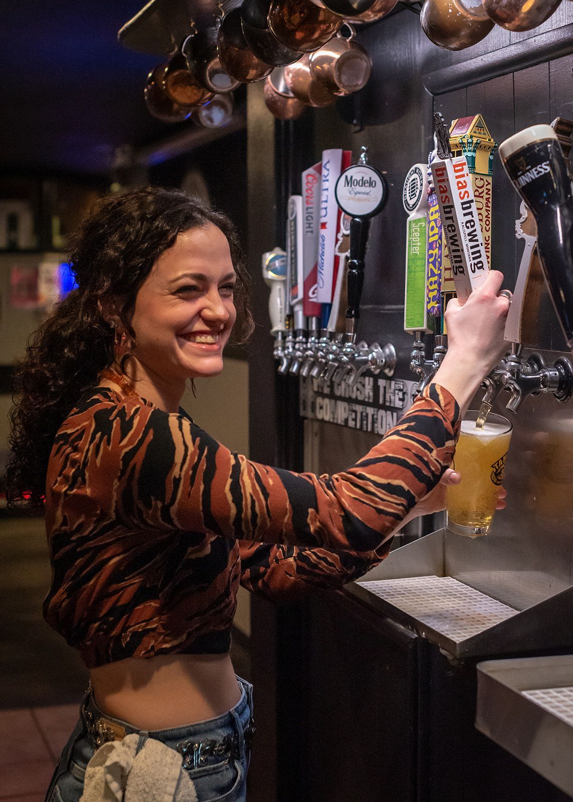 A woman is pouring a beer from a tap in a bar.