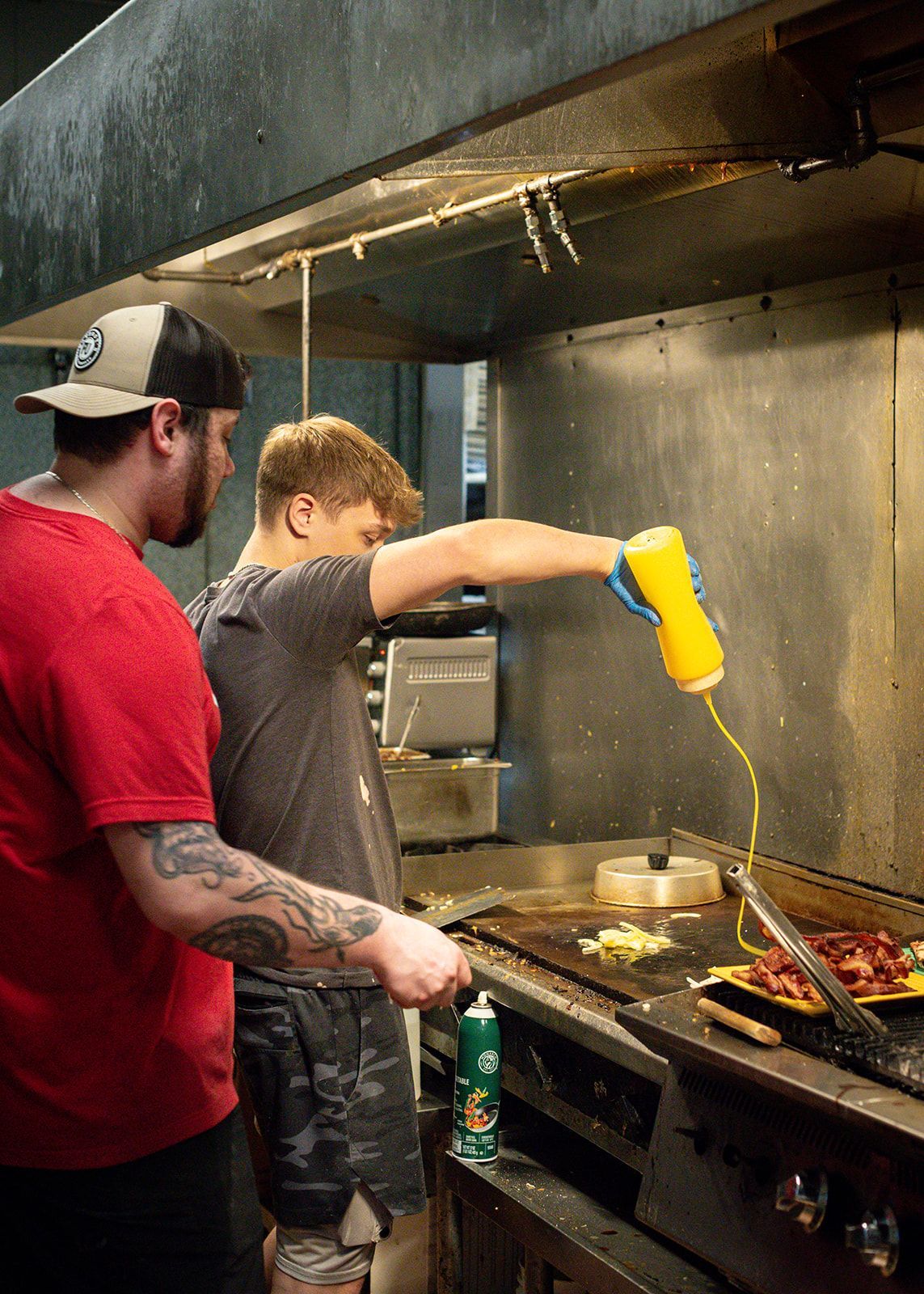 Two men are cooking food on a grill in a kitchen.