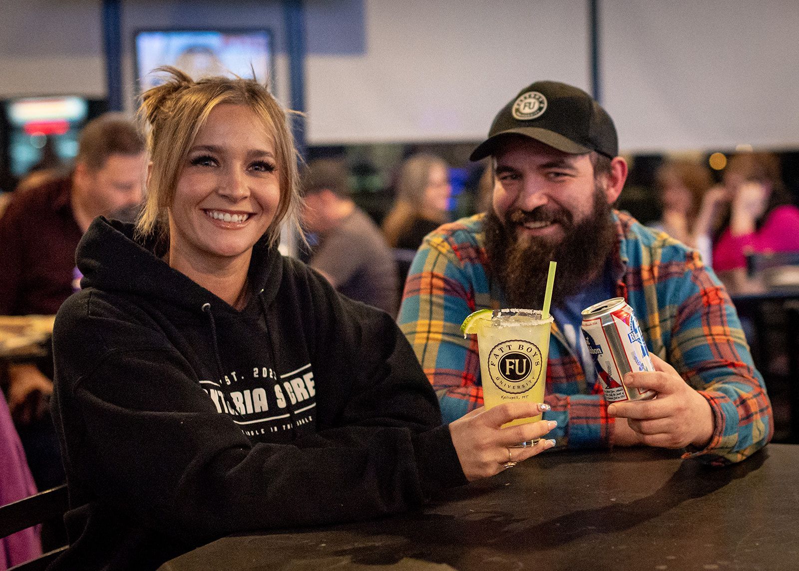 A man and a woman are sitting at a table holding drinks.