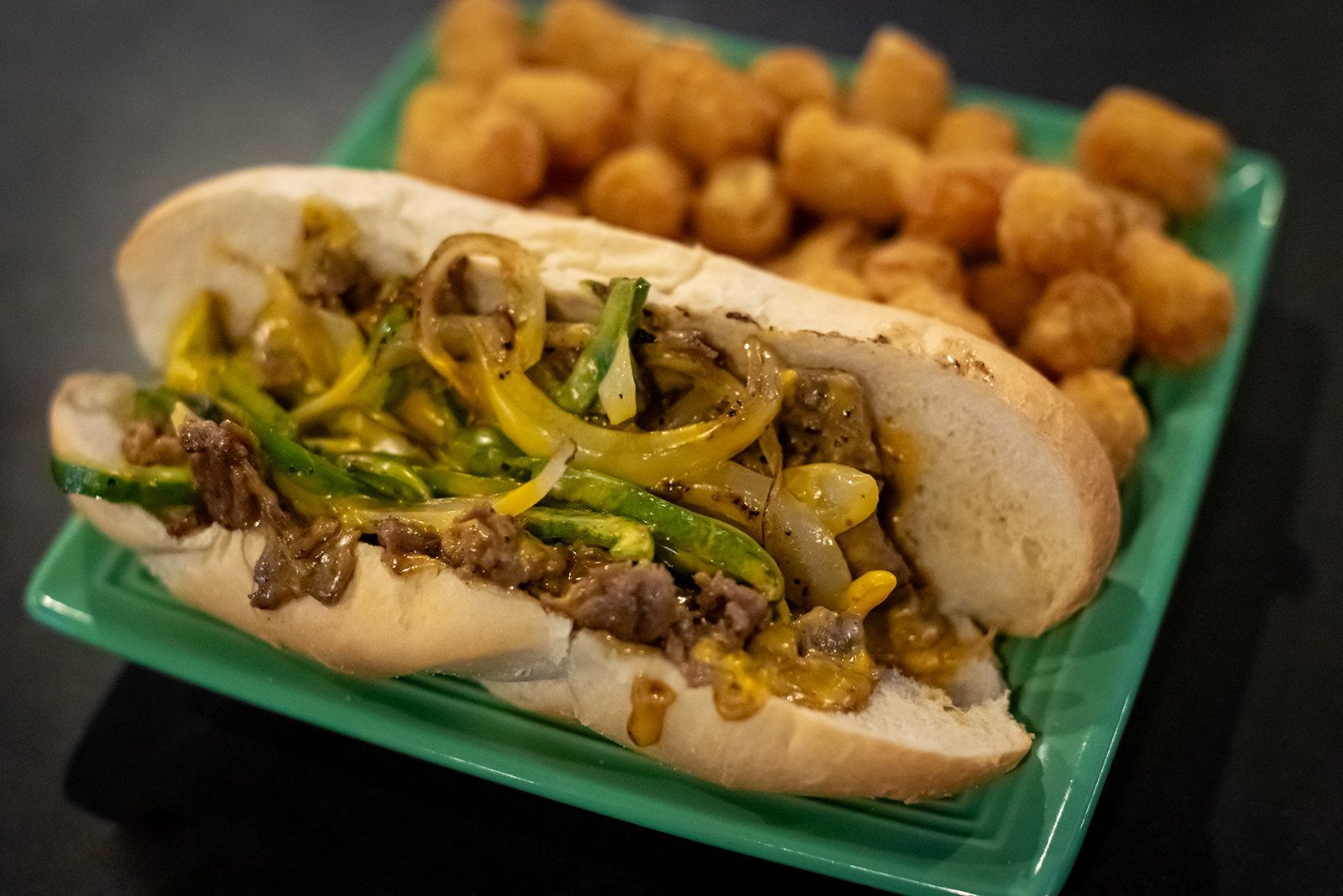 A sandwich and tater tots on a green plate