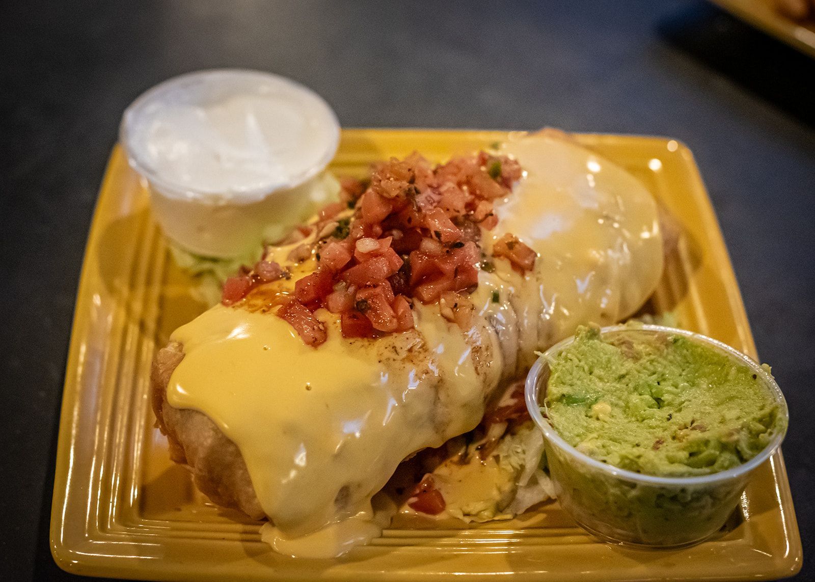A burrito with guacamole and sour cream on a yellow plate.