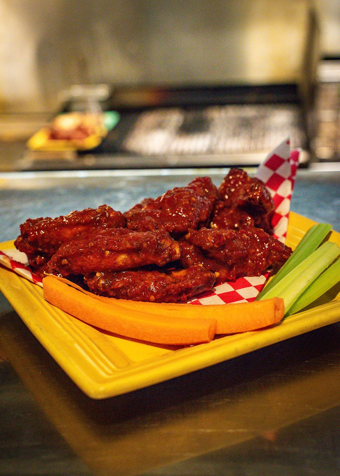 A yellow plate topped with chicken wings and celery sticks.