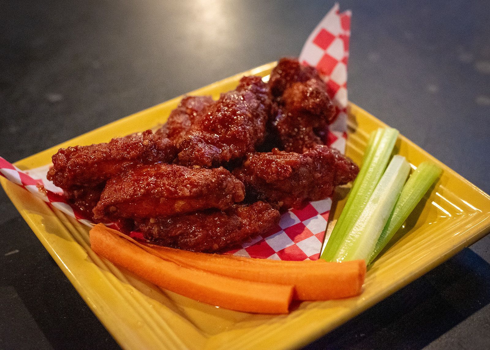 A yellow plate topped with chicken wings , carrots and celery.