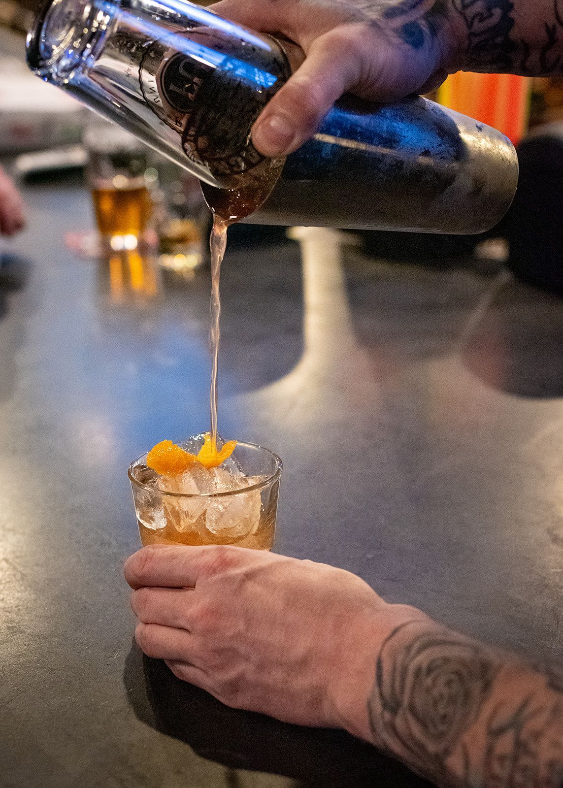 A bartender is pouring a drink into a glass with ice.