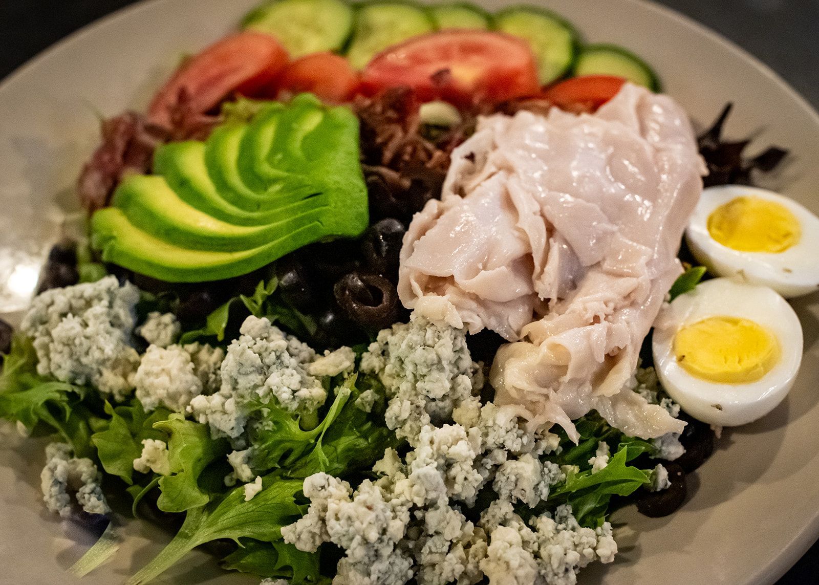 A salad with avocado , turkey , eggs , blue cheese and olives on a plate.