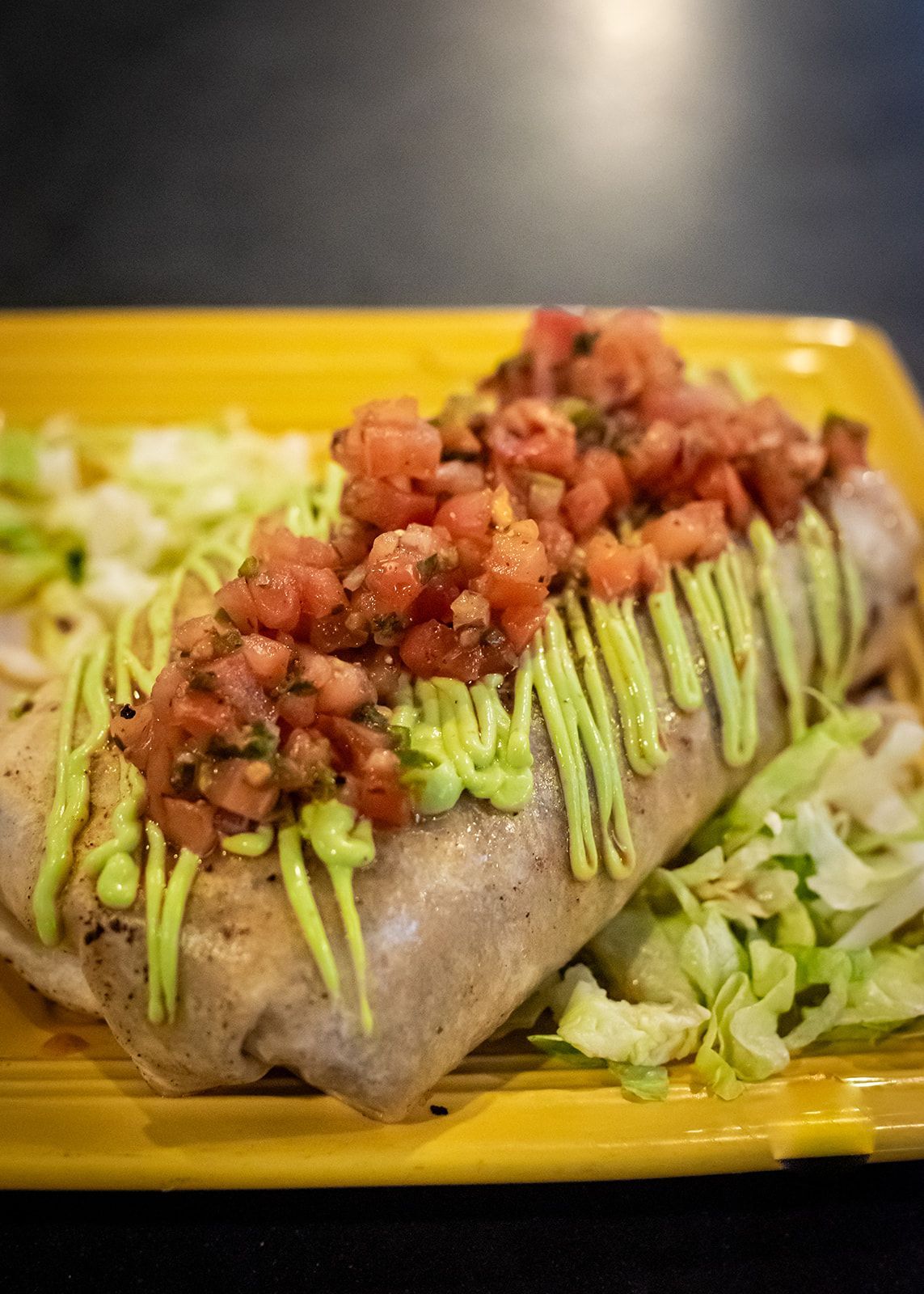 A burrito with tomatoes , lettuce and guacamole on a yellow plate.