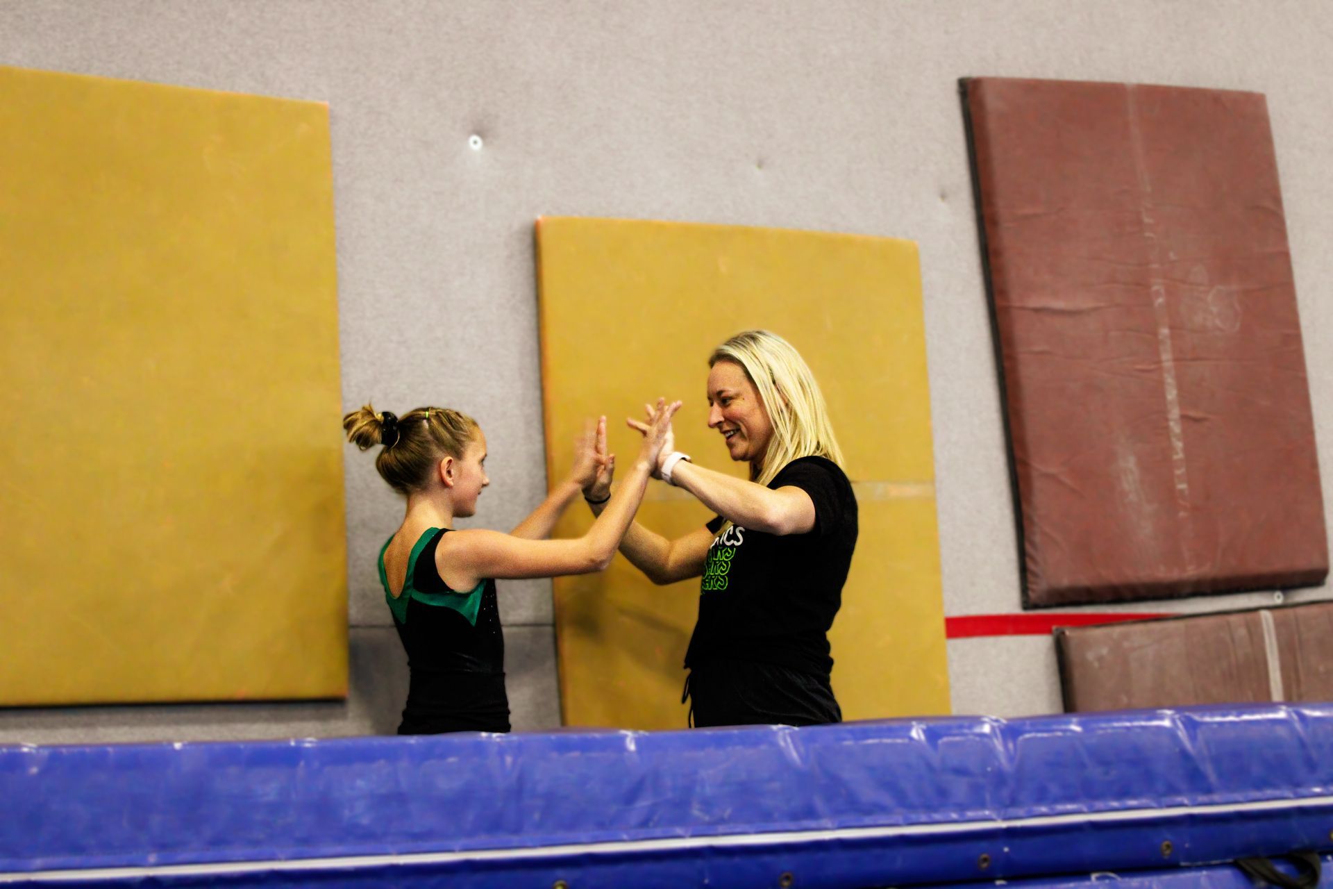 Two people practicing a hand-clap routine in a gym with padded walls and a blue mat in front