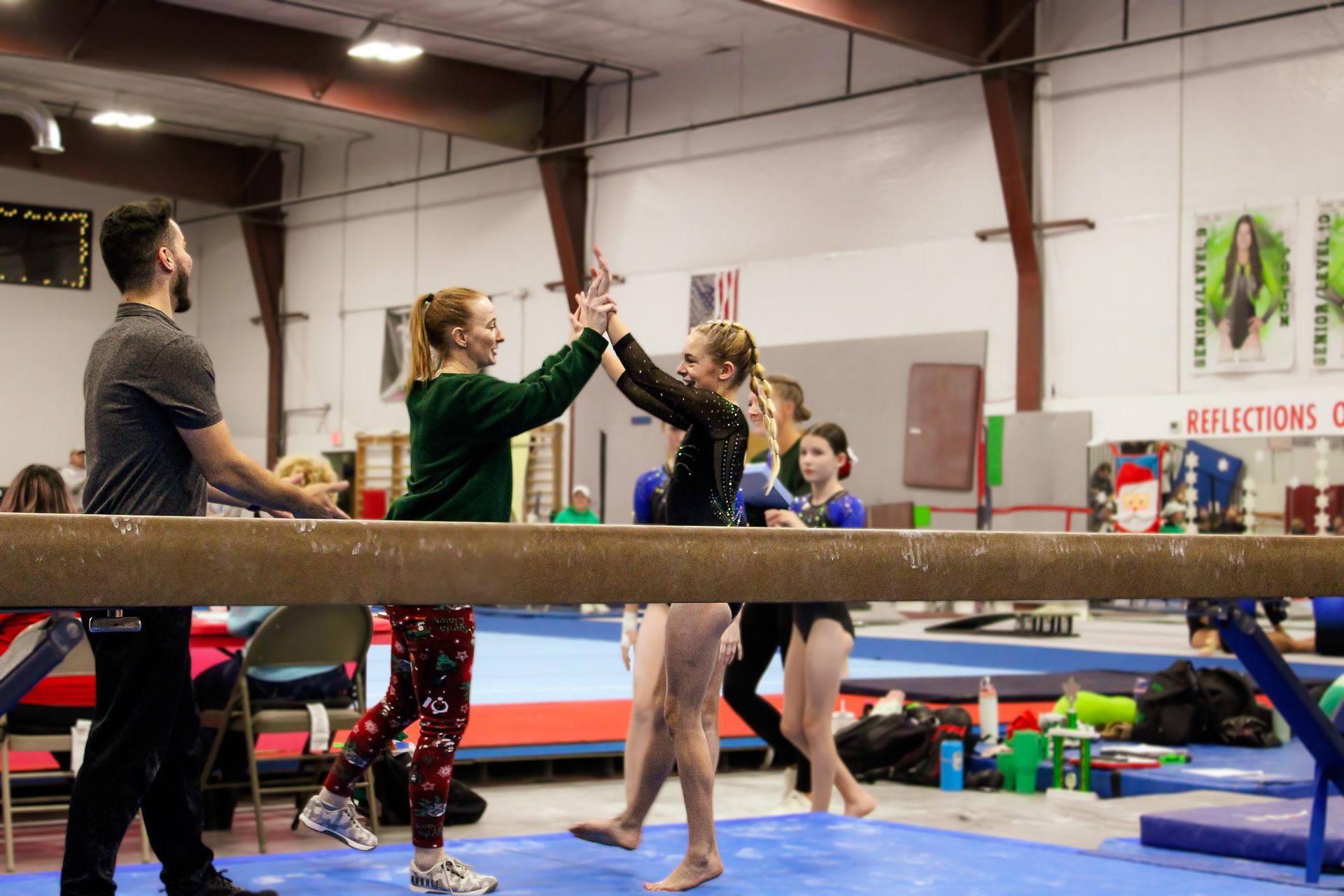 People high-five in a gymnastics gym with mats and balance beams visible.