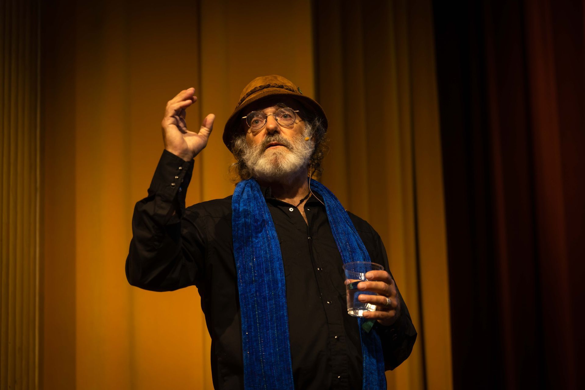 A man with a beard is holding a glass of water on a stage.