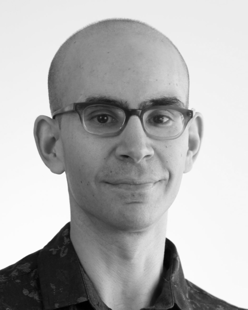A bald man wearing glasses is smiling in a black and white photo.