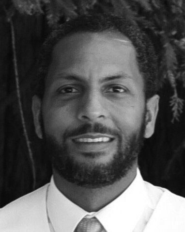 A black and white photo of a man with a beard wearing a white shirt and tie.