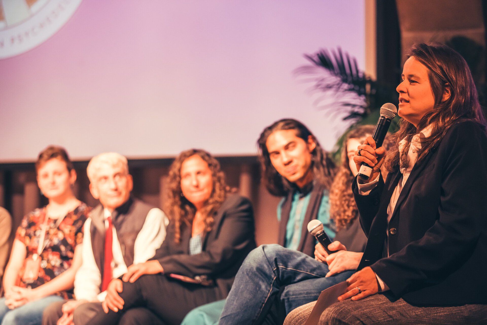 A group of people are sitting on a stage with a woman holding a microphone.