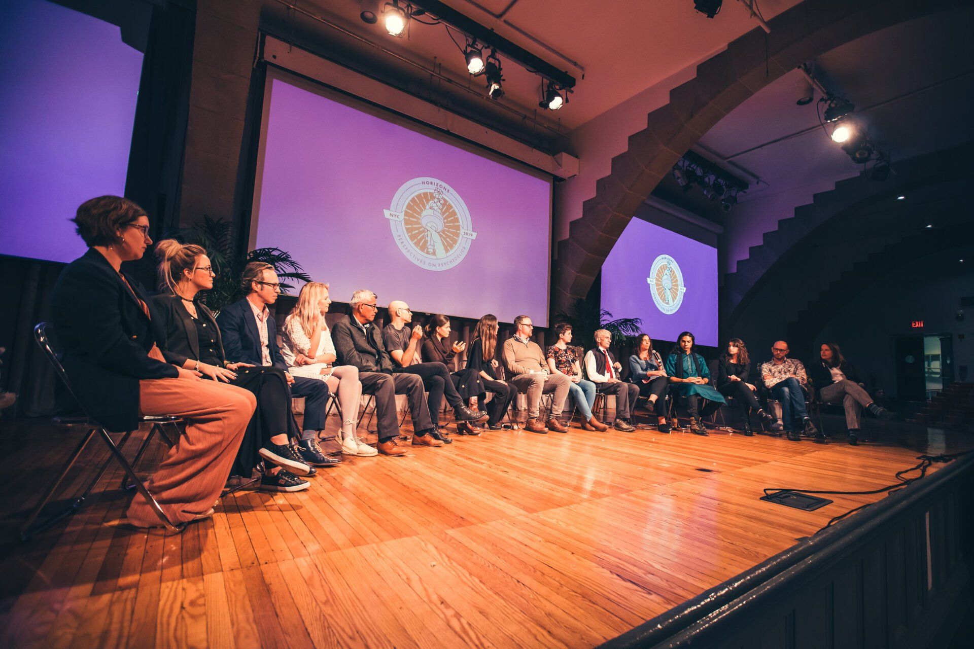 A group of people are sitting on a stage in front of a large screen.