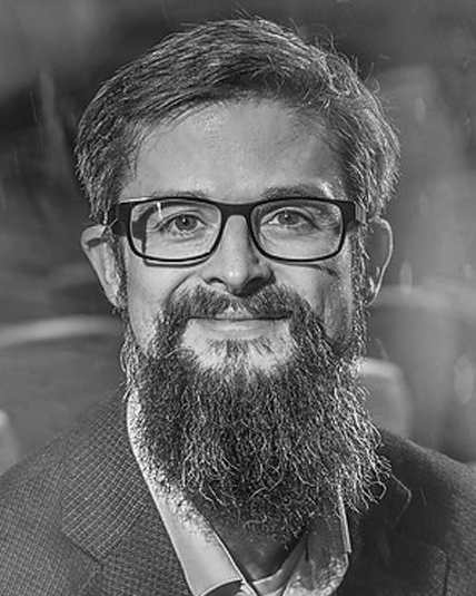 A man with a beard and glasses is wearing a suit and tie.