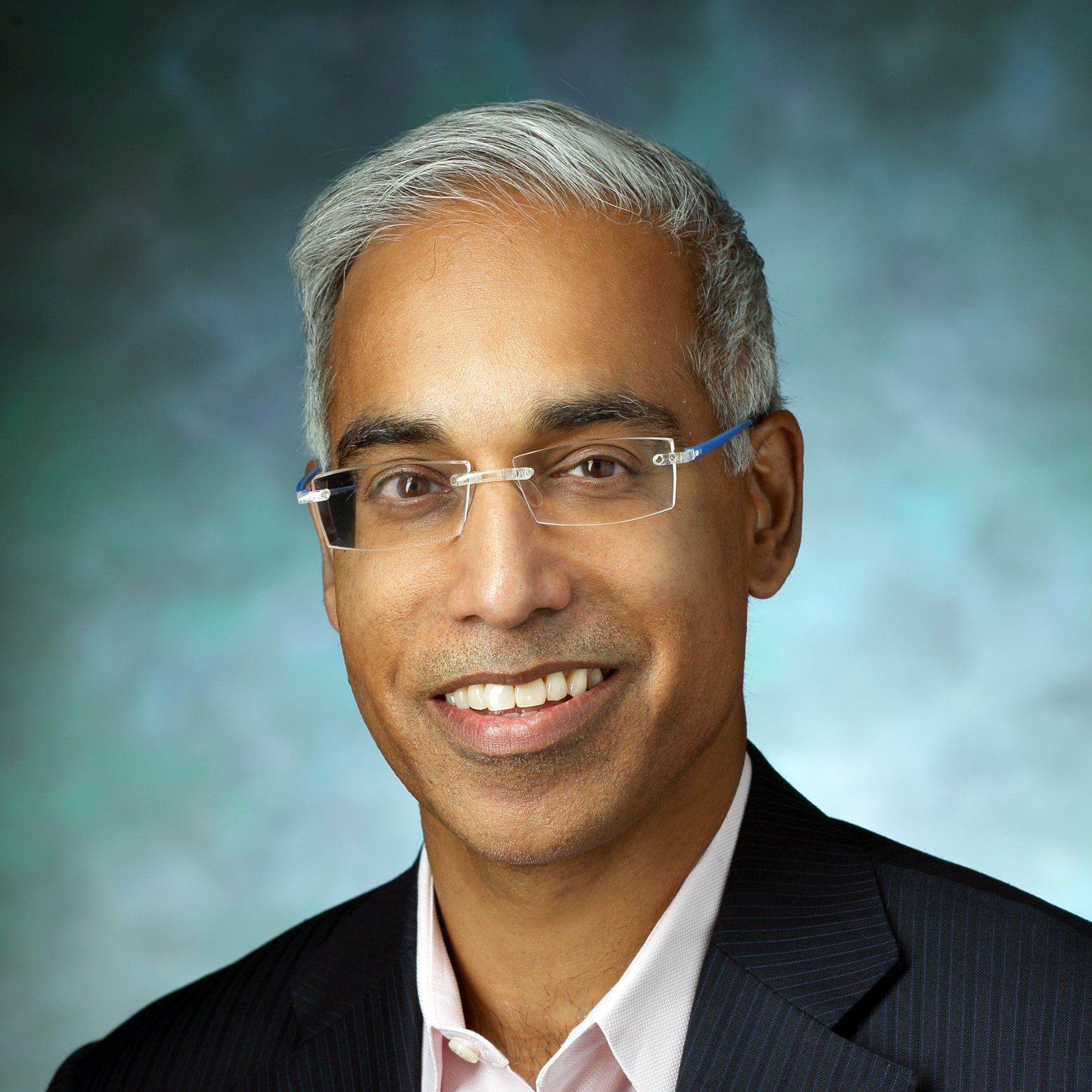 A man wearing glasses and a suit is smiling for the camera.