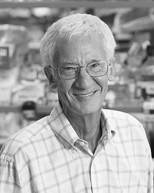 A black and white photo of an older man wearing glasses and a plaid shirt.