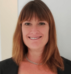 A woman wearing a necklace and a black jacket smiles for the camera