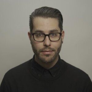 A man with glasses and a beard is wearing a black shirt.