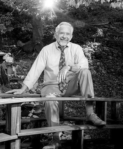 A black and white photo of a man sitting on a bench.